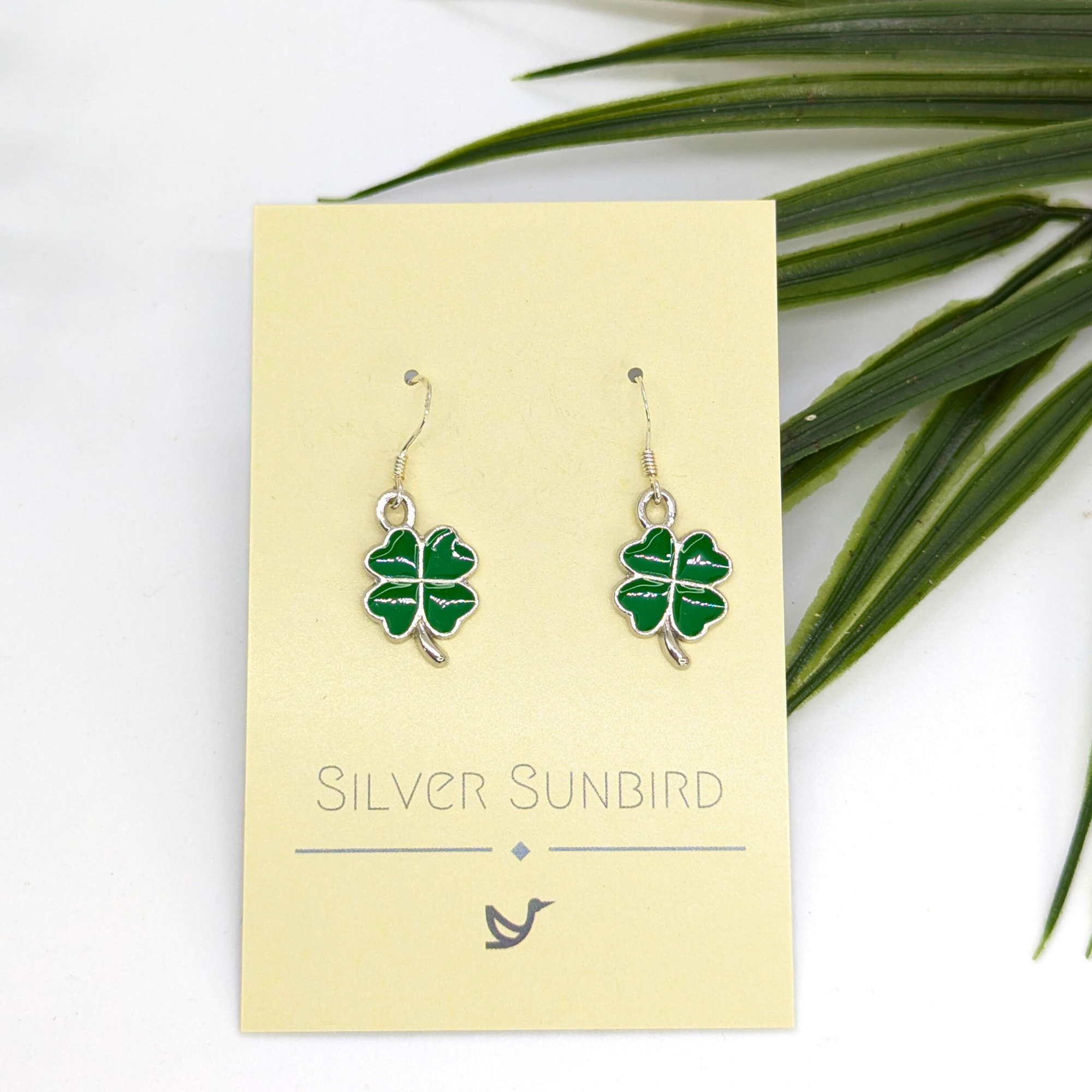 A pair of Lucky Four Leaf Clover Earrings by Silver Sunbird, displayed on a branded card with green leaves visible in the top right corner.