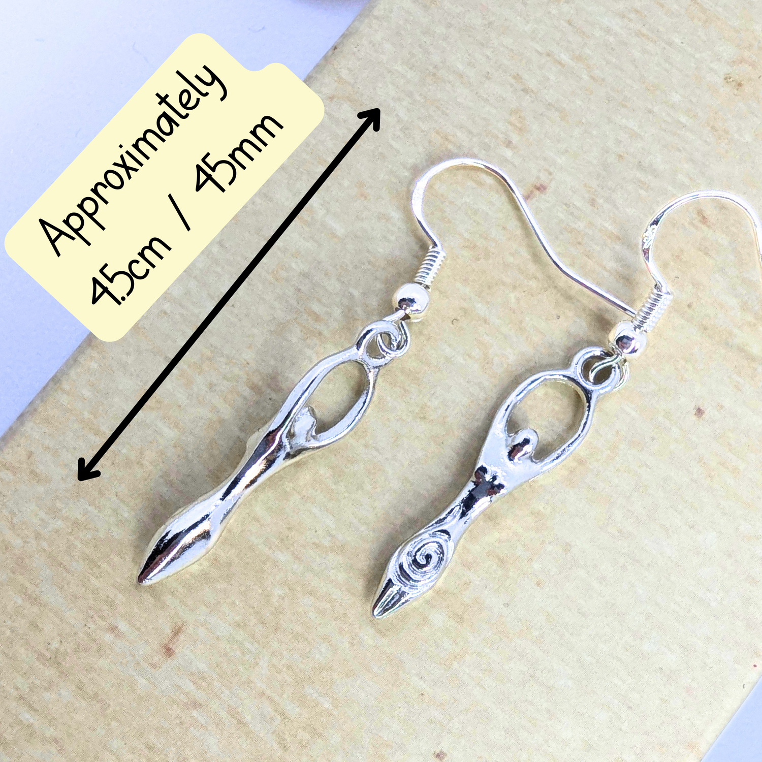 The Silver Sunbird Fertility Goddess Dangle Earrings feature stylized goddess figures, each 4.5 cm (45 mm) long, handmade and beautifully displayed on a light surface.
