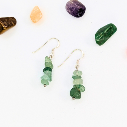 The Silver Sunbird Green Aventurine Earrings feature stacked gemstone chips with sterling silver hooks, showcased on a white surface and surrounded by colorful stones—ideal for handmade gemstone jewelry lovers.