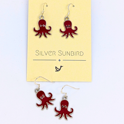 Red Octopus Earrings by Silver Sunbird feature an enamel finish and silver hooks, designed as ocean-inspired jewelry. Displayed on and below a branded &quot;Silver Sunbird&quot; card.