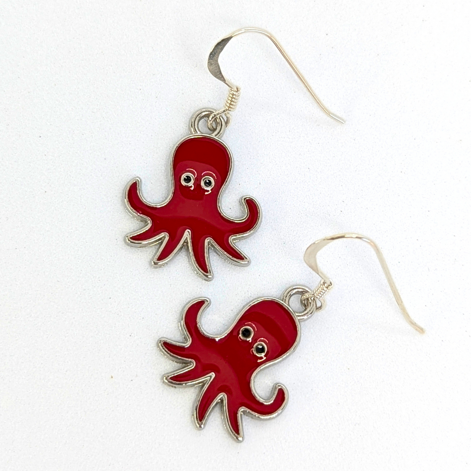 The Silver Sunbird Red Octopus Earrings feature big-eyed red charms on sterling silver, perfect for ocean-inspired jewelry lovers and shown on a white background.
