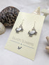 Displayed on a card with seashells, the "Silver Sunbird" Coastal Crab Earrings are sterling silver, crab-shaped, and hypoallergenic for comfort. These earrings bring seaside charm to any attire and offer a stylish nod to the coast.