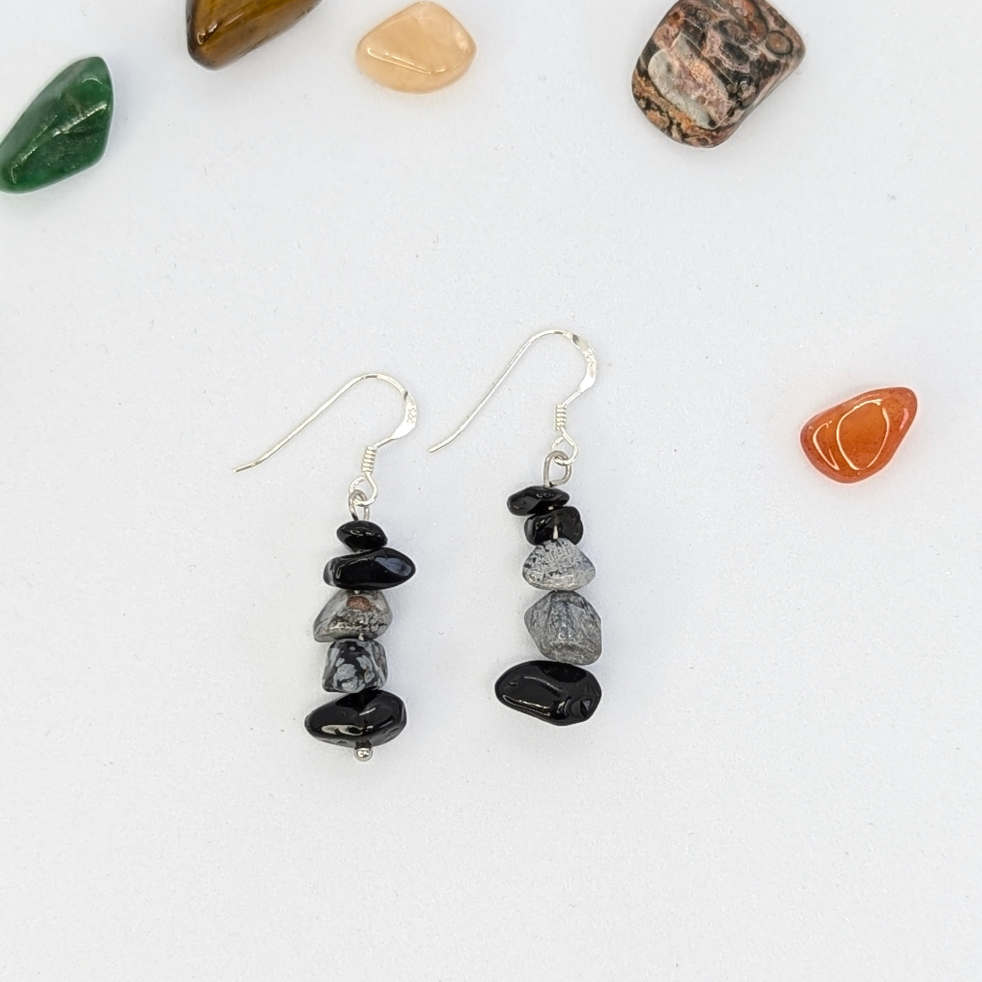 The Silver Sunbird Snowflake Obsidian Earrings feature stacked black and gray stones on silver hooks, accented with polished gemstones—perfect for fans of handmade crystal jewelry.