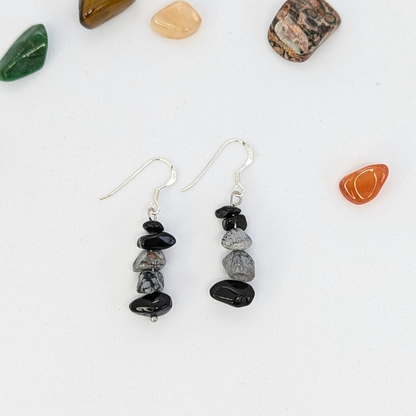 The Silver Sunbird Snowflake Obsidian Earrings feature stacked black and gray stones on silver hooks, accented with polished gemstones—perfect for fans of handmade crystal jewelry.