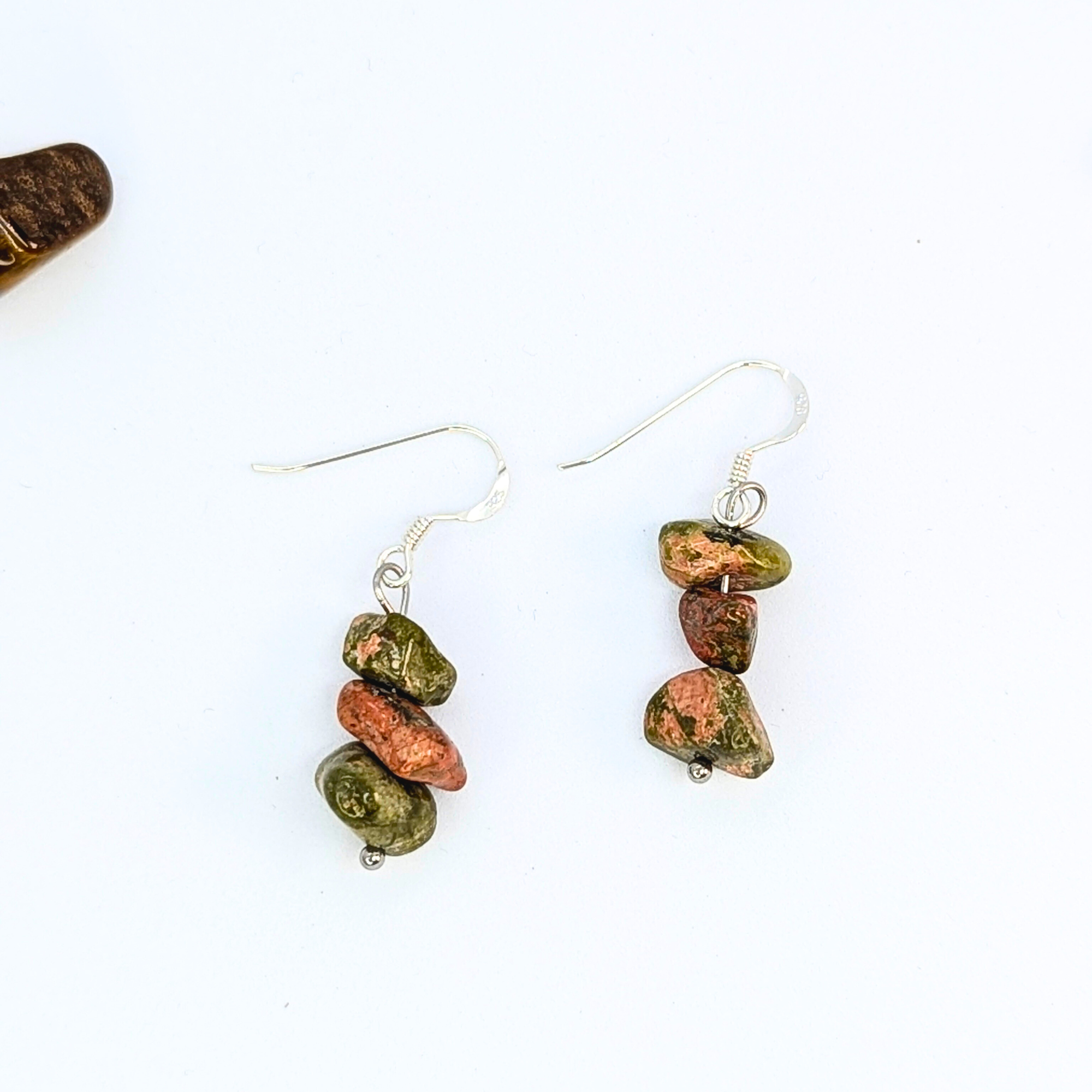 The Unakite Gemstone Earrings by Silver Sunbird feature three stacked green and reddish-brown stone beads with silver hooks, offering a unique handmade design and earthy charm.