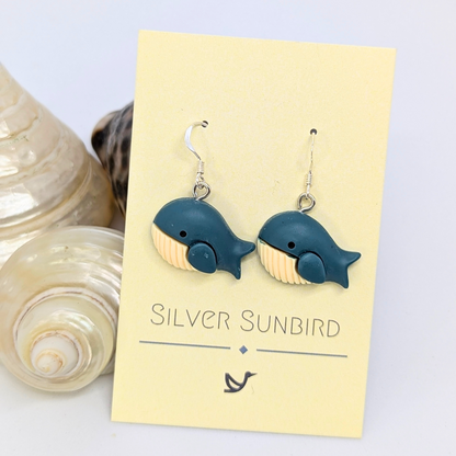 Colourful Whale Earrings by Silver Sunbird in blue and beige, displayed on a branded card with seashells—perfect nautical jewelry for ocean lovers.