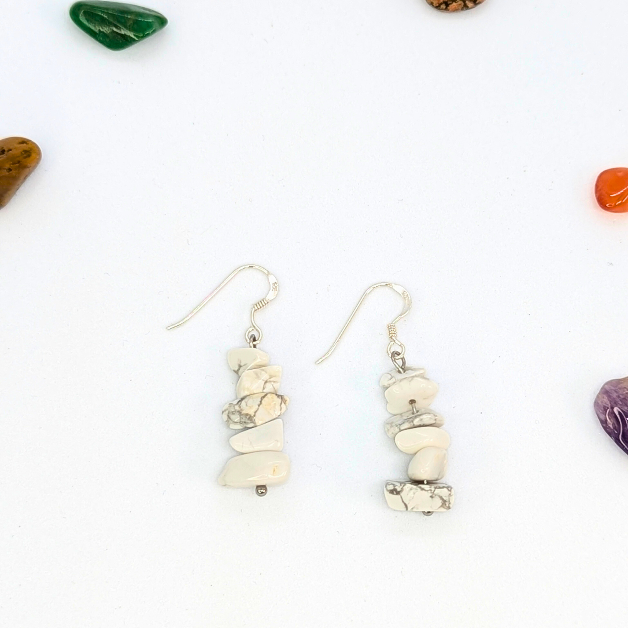 Silver Sunbird’s White Howlite Gemstone Earrings, featuring stacked marbled stones, are displayed on a white surface with colorful tumbled stones—an ideal choice for handmade jewellery enthusiasts.