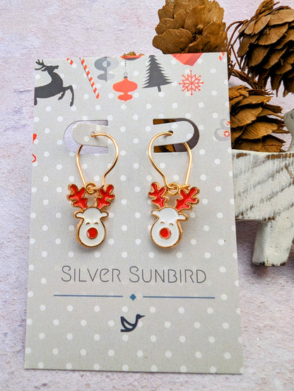 A pair of Rosie Reindeer Hoop Earrings by Silver Sunbird, showcasing festive enamel with red antlers and gold details, is elegantly displayed on a decorative card amidst small pine cones.