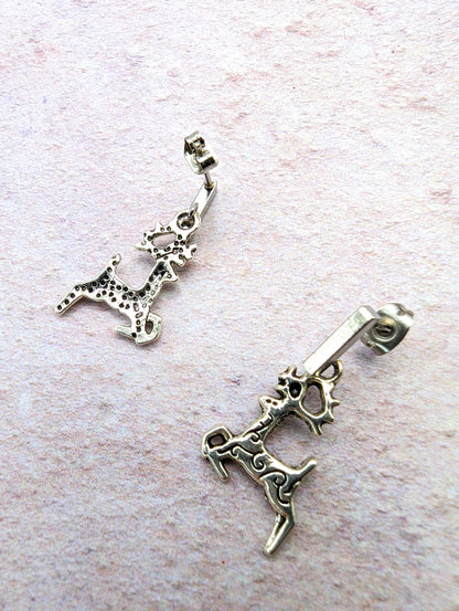 A pair of Prancing Reindeer Earrings from Silver Sunbird, crafted from stainless steel with a rustic, antique finish and intricate detailing, lies on a textured, light-colored surface. These playful and dynamic earrings add charm to your collection of handmade jewelry.