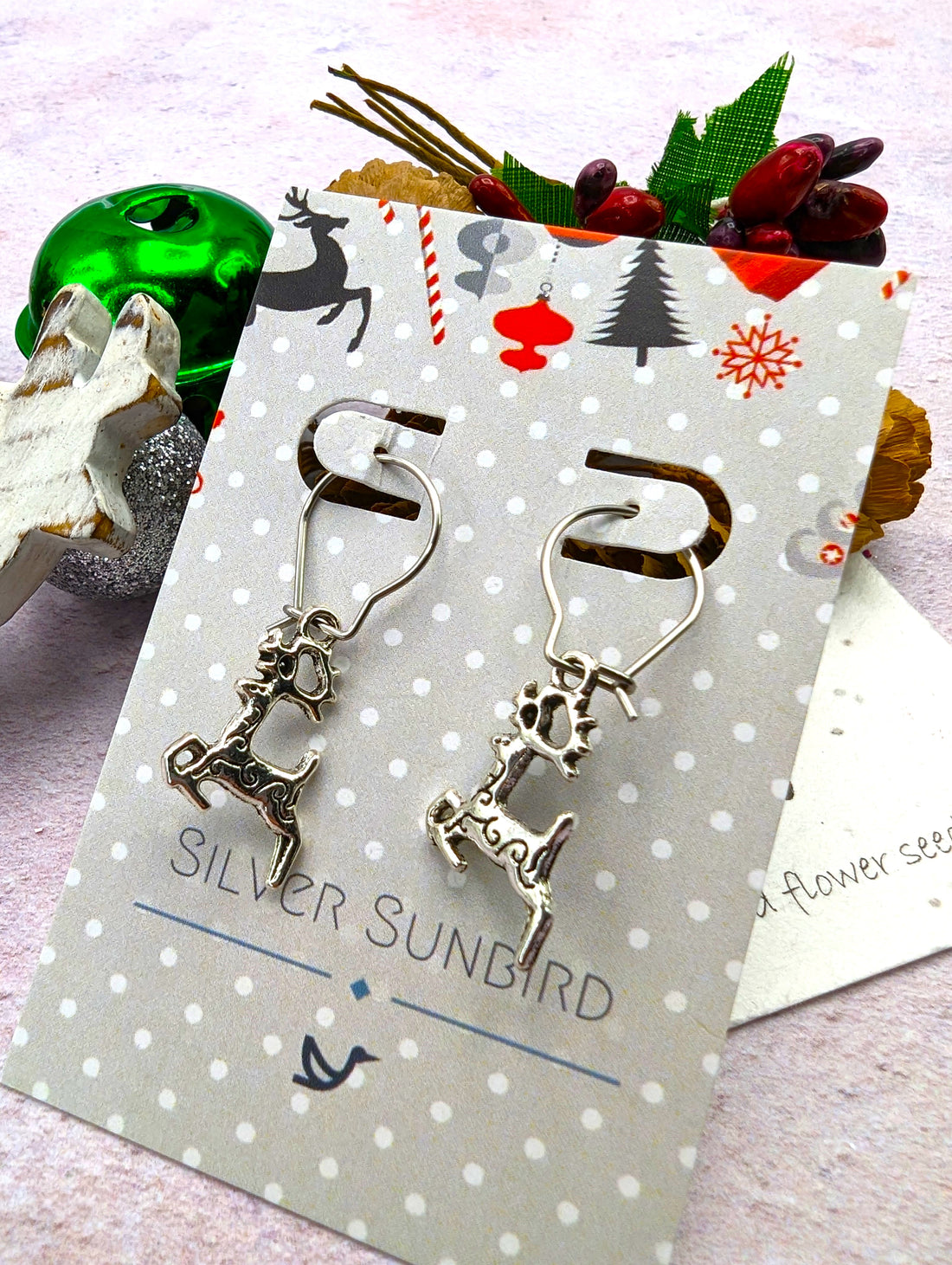 The Prancing Reindeer Earrings from Silver Sunbird, crafted from stainless steel, rest on a polka-dotted card featuring the brand&