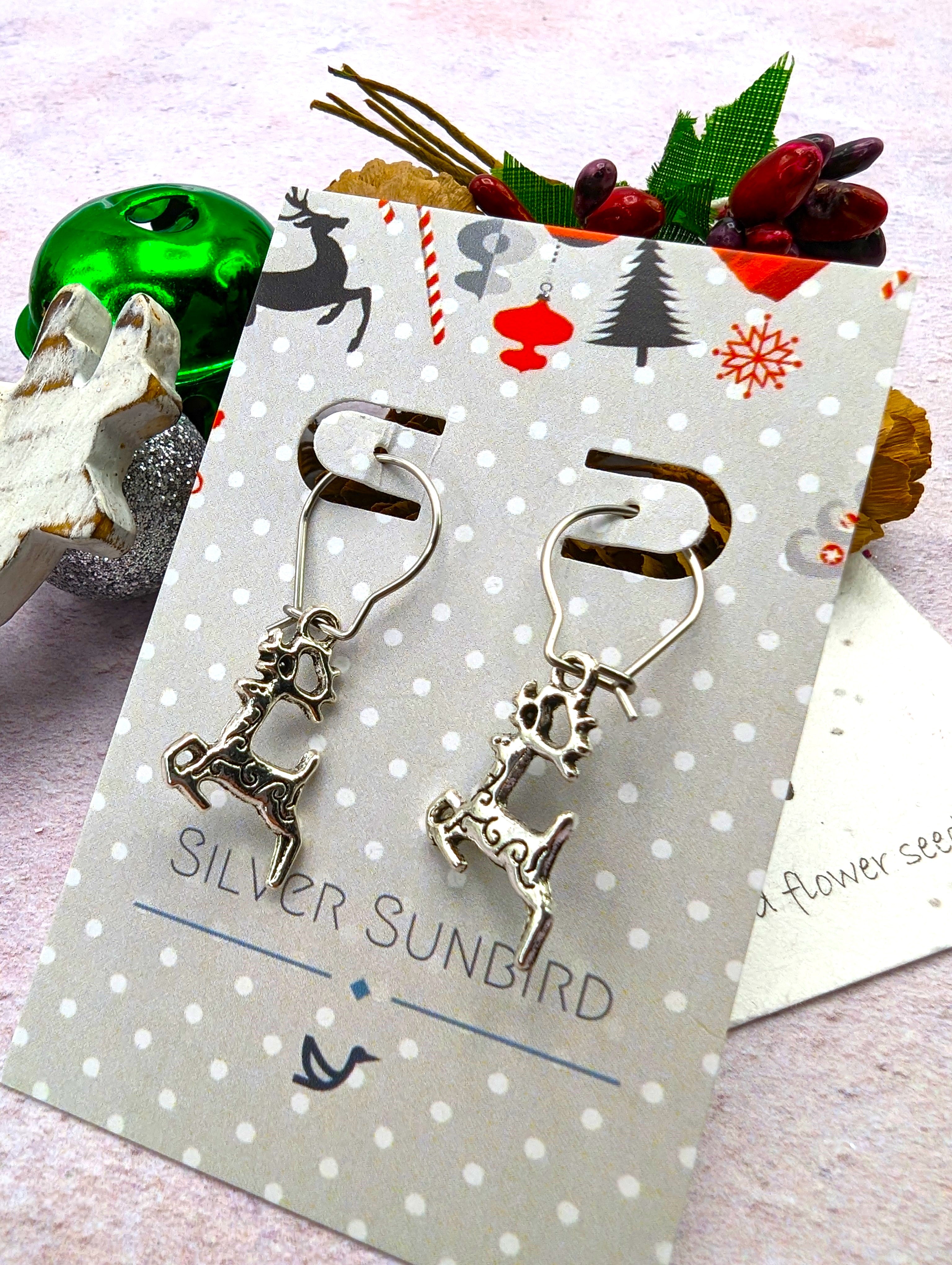 The Prancing Reindeer Earrings from Silver Sunbird, crafted from stainless steel, rest on a polka-dotted card featuring the brand&